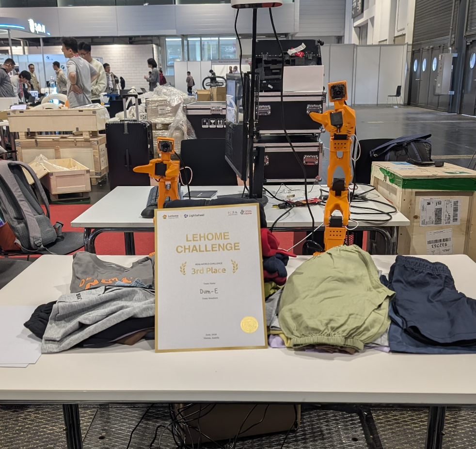 LeHome Challenge finals setup with the certificate, robot arms, and garments.